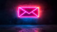 Glowing neon mail envelope sign on dark concrete wall with pink and blue light reflection on wet floor. Modern communication concept for business design.