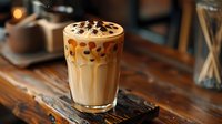 Creamy iced coffee drink with chocolate chips and whipped cream topping served in tall glass on wooden board, caramel drizzle streaming down sides in cafe setting.
