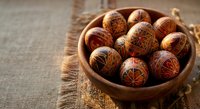 Traditional decorated Easter eggs in wooden bowl on rustic burlap fabric background showcasing intricate folk art patterns and warm brown tones for holiday celebrations.