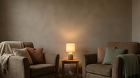 Cozy living room interior with two comfortable armchairs, warm table lamp lighting, and neutral earth tone color palette creating relaxing home atmosphere.