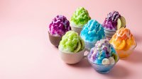 Colorful shaved ice desserts in cups with various bright flavors including purple, green, blue, and orange on pink background. Isolated design element.