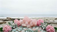 Large rose quartz crystal cluster with pink hydrangea flowers on driftwood by ocean shore for healing meditation and spiritual wellness practices.
