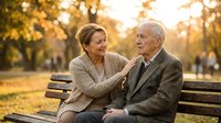 Happy senior couple sitting on park bench during golden hour sunset, elderly man and woman sharing intimate moment outdoors in autumn, retirement lifestyle.