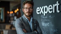 Confident professional businessman wearing glasses and gray suit jacket poses with crossed arms against modern office wall with text display, perfect for business and leadership concepts.