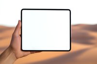 Female hand holding modern tablet device with blank white screen against blurred desert sand dunes background, mockup for digital presentation.