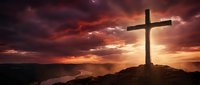 Wooden cross silhouetted against dramatic sunset sky with vibrant red and orange clouds over mountainous landscape for spiritual and religious themes.