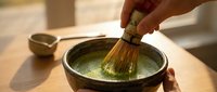 Whisk being stirred in green matcha tea powder in ceramic bowl during traditional Japanese tea ceremony preparation.