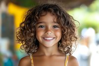 Young girl with curly brown hair and bright smile wearing yellow dress, outdoor portrait for children's advertising, education, and family lifestyle content.