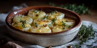 Baked potato gratin with cream sauce and fresh thyme in rustic ceramic dish, golden brown crust on top, moody food photography with natural lighting.