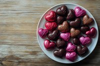 Assorted chocolate candies in heart shapes and round truffles arranged on white plate, wooden table background for Valentine's Day celebration and romantic gifts.