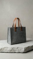 Gray felt tote bag with cognac leather handles, displayed on stone platform. Minimalist design suitable for fashion, retail, and lifestyle marketing materials.