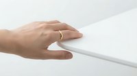 Woman's hand with gold ring touching white tablet device on neutral background, technology and modern gadget interaction.