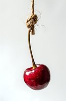 Fresh ripe red cherry hanging by knotted stem against white background, minimalist food photography composition for culinary and design projects.