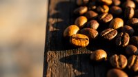 Roasted coffee beans scattered on rustic wooden surface with warm golden lighting creating cozy cafe atmosphere for beverage and food concepts.