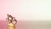 Elegant golden perfume bottle with ornate decorative cap on soft pink gradient background for luxury cosmetics and fragrance advertising campaigns.