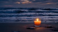 Glowing candle on sandy beach at twilight with ocean waves and dramatic sunset sky creating peaceful meditation atmosphere for relaxation and mindfulness.
