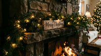 Cozy stone fireplace adorned with glowing garland and a wooden Merry Christmas sign, warm holiday home decor with festive lights.