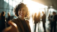 Young professional woman with curly hair smiling in bright corporate environment with blurred colleagues in background, conveying confidence and success.