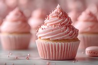 Pink vanilla cupcake with swirled buttercream frosting topped with metallic sugar pearls and sprinkles on light background with soft bokeh effect.