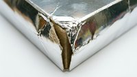 Shiny metallic silver foil wrapping paper with torn corner revealing brown cardboard underneath, close-up detail of damaged packaging material.
