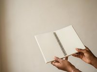 Open spiral notebook with blank pages held by hands with medium skin tone against neutral beige background, suitable for education, planning, writing, and creative projects.