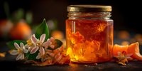 Golden honey jar with orange blossom flowers on rustic wooden surface. Natural organic sweetener with floral elements for culinary and wellness uses.