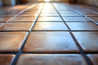Close-up view of terracotta floor tiles with dark grout lines creating geometric pattern, shot with shallow depth of field in warm natural lighting.