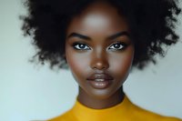 Young African woman with natural curly afro hair and glowing skin wearing yellow turtleneck sweater against light background, close up beauty portrait.