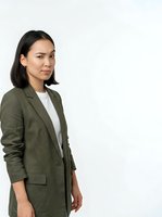 Young woman with long dark hair and East Asian ethnicity wearing olive green blazer over white shirt, standing against white background for corporate and business use.