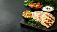Grilled flatbread served with fresh tomato salsa, white sauce and corn salad on dark wooden board. Traditional Middle Eastern cuisine with herbs and dips.
