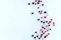 Small red and black heart shapes scattered on white background creating curved pattern, minimalist romantic design for valentines cards and love concepts.