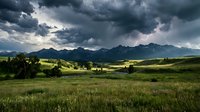 Dramatic stormy sky looms over lush green valley with distant mountains, meadow landscape for nature and weather backgrounds.