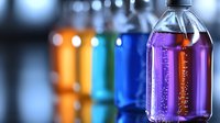Colorful liquid-filled bottles in row with bubbles and reflections against blurred background, showcasing vibrant purple, orange, blue and green hues for beverage industry.