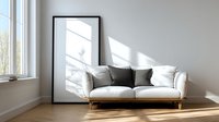 Modern white sofa with gray pillows in bright minimalist living room interior with large black frame and window casting natural sunlight shadows.