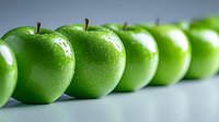 Fresh green apples with water drops arranged in row on light background. Clean composition showing natural organic produce for healthy eating concept.