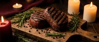 Grilled beef steak with herbs and spices on wooden board surrounded by candles creating warm atmospheric dining ambiance for restaurant menu design.