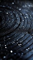 Macro shot of dark concentric circles with water droplets and bokeh light effects creating mysterious atmospheric background for luxury product photography.