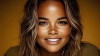 Young African American woman with highlighted wavy hair and radiant smile against golden background, wearing casual top, showcasing natural beauty and confidence.