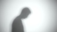 Blurred shadow silhouette of person with head down against white wall suggesting depression, loneliness or contemplation for mental health concepts.