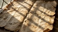 Ancient weathered parchment manuscript with torn edges and natural aging, illuminated by warm sunlight creating dramatic shadows for historical designs.