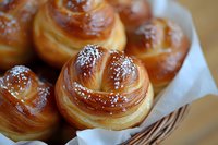 Fresh homemade sweet buns with golden brown crust sprinkled with powdered sugar, served in rustic basket with white cloth, close up view of pastries.