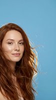 Young Caucasian woman with flowing auburn hair against blue background, natural beauty portrait for skincare and haircare advertising campaigns.