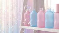 Colorful baby bottles in pink and blue arranged on white shelf with soap bubbles floating in soft pastel nursery room for infant feeding and childcare.