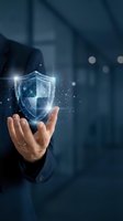 Businessman holding glowing digital shield with particles in modern office environment, representing cybersecurity, data protection, and network security solutions.