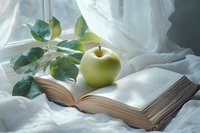 Fresh green apple on open book with green plant leaves against white fabric, creating serene reading atmosphere in natural morning light.