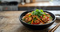Asian stir-fry with beef, vegetables and noodles in black pan on wooden table. Fresh cilantro garnish adds color to this appetizing meal ready to serve.