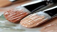 Macro shot of professional makeup brushes with cream foundation or concealer product, showing detailed bristles and texture for cosmetic application.