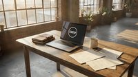 Laptop with startup text on screen sits on wooden desk in sunlit loft workspace with brick walls, coffee cup, and scattered documents.