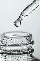 Glass dropper with water droplets dispensing liquid into laboratory beaker for scientific research and medical testing applications.