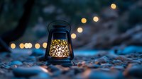 Glowing decorative lantern with intricate pattern on rocky beach at dusk, warm light illuminating pebbles against blurred bokeh background creates cozy atmosphere.